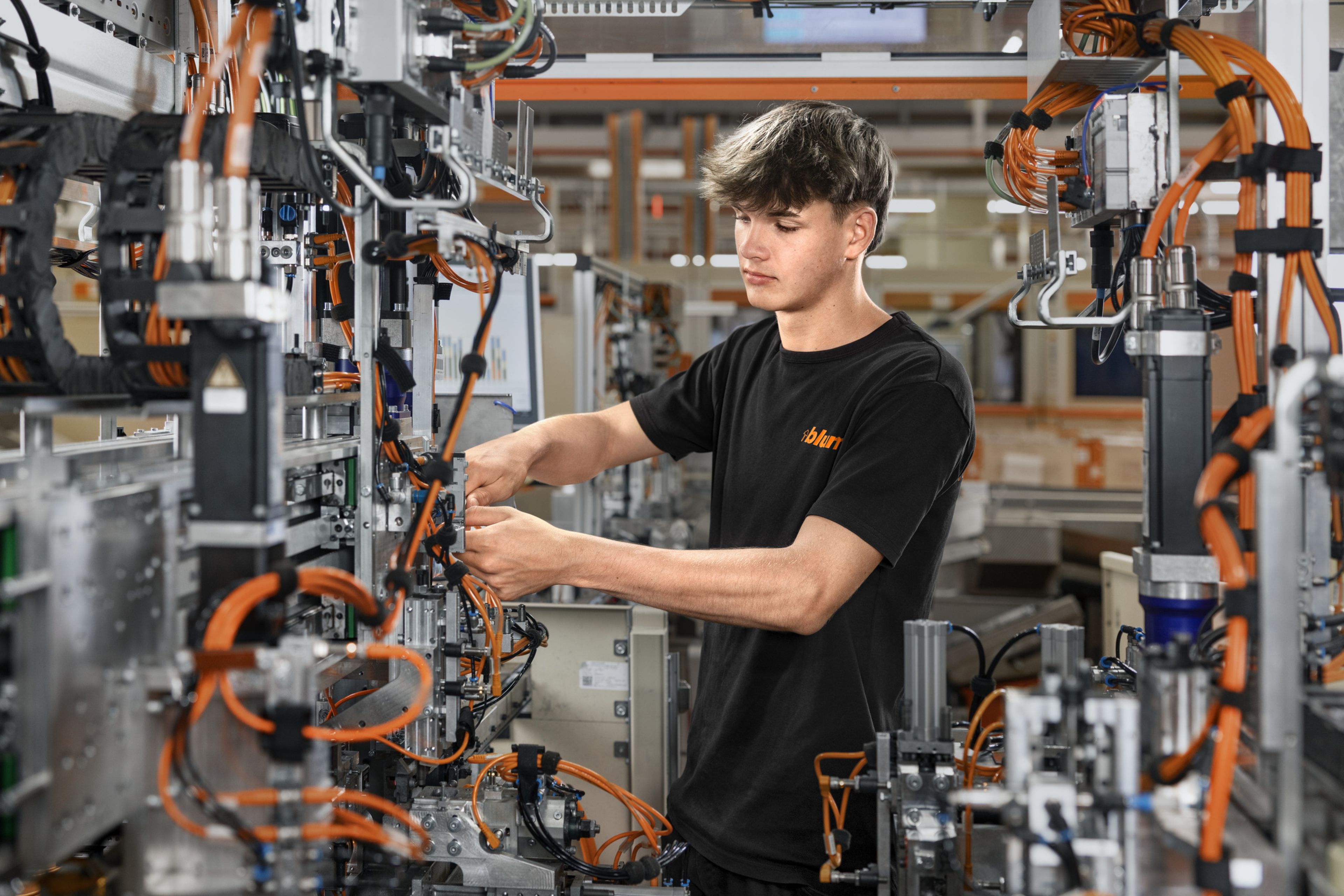 Das Bild zeigt einen männlichen Lehrling in der Mechatronik bei Blum, der in einer Anlage arbeitet. 