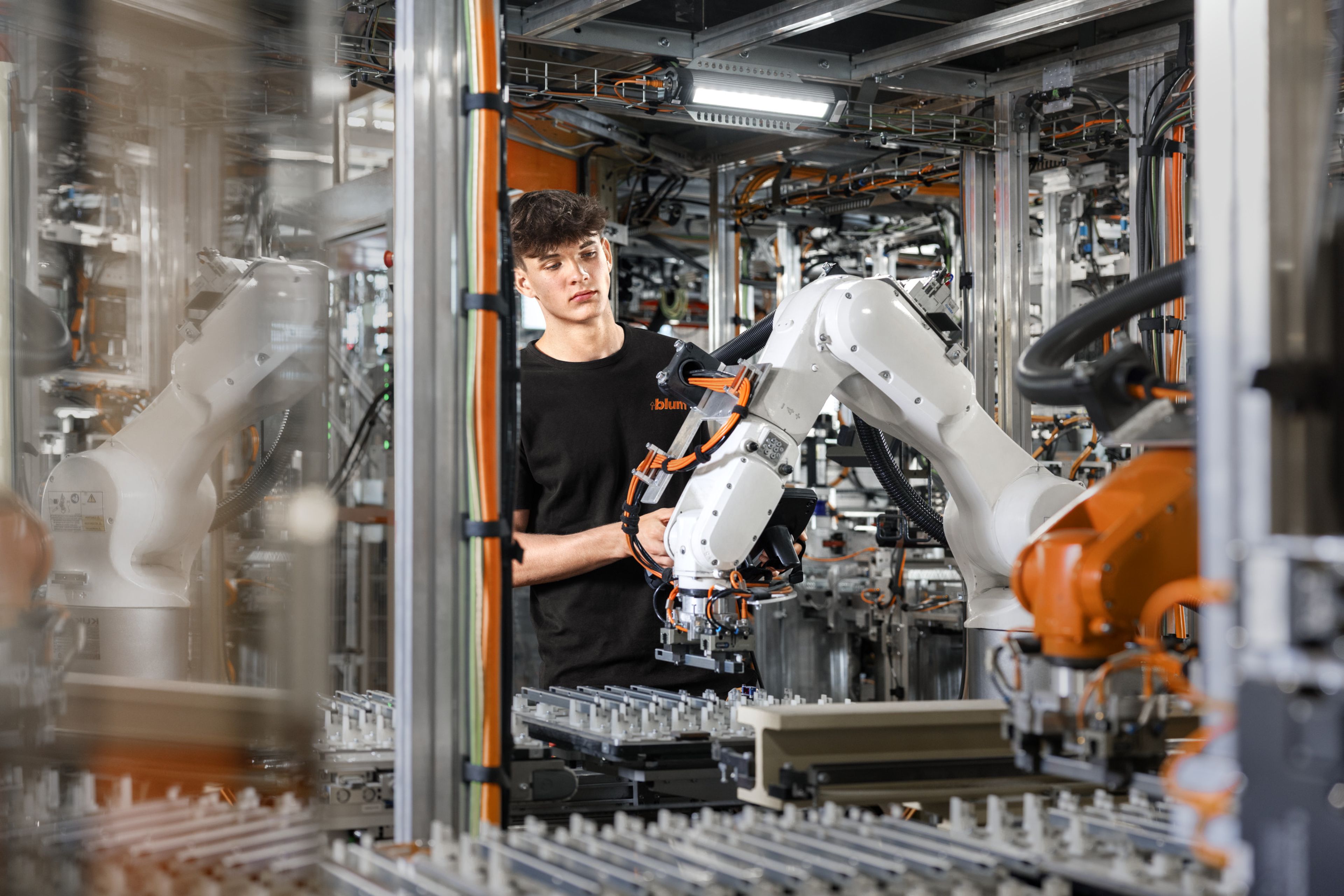 Das Bild zeigt einen männlichen Lehrling in der Mechatronik bei Blum, der in einer Anlage einen Roboter steuert. 