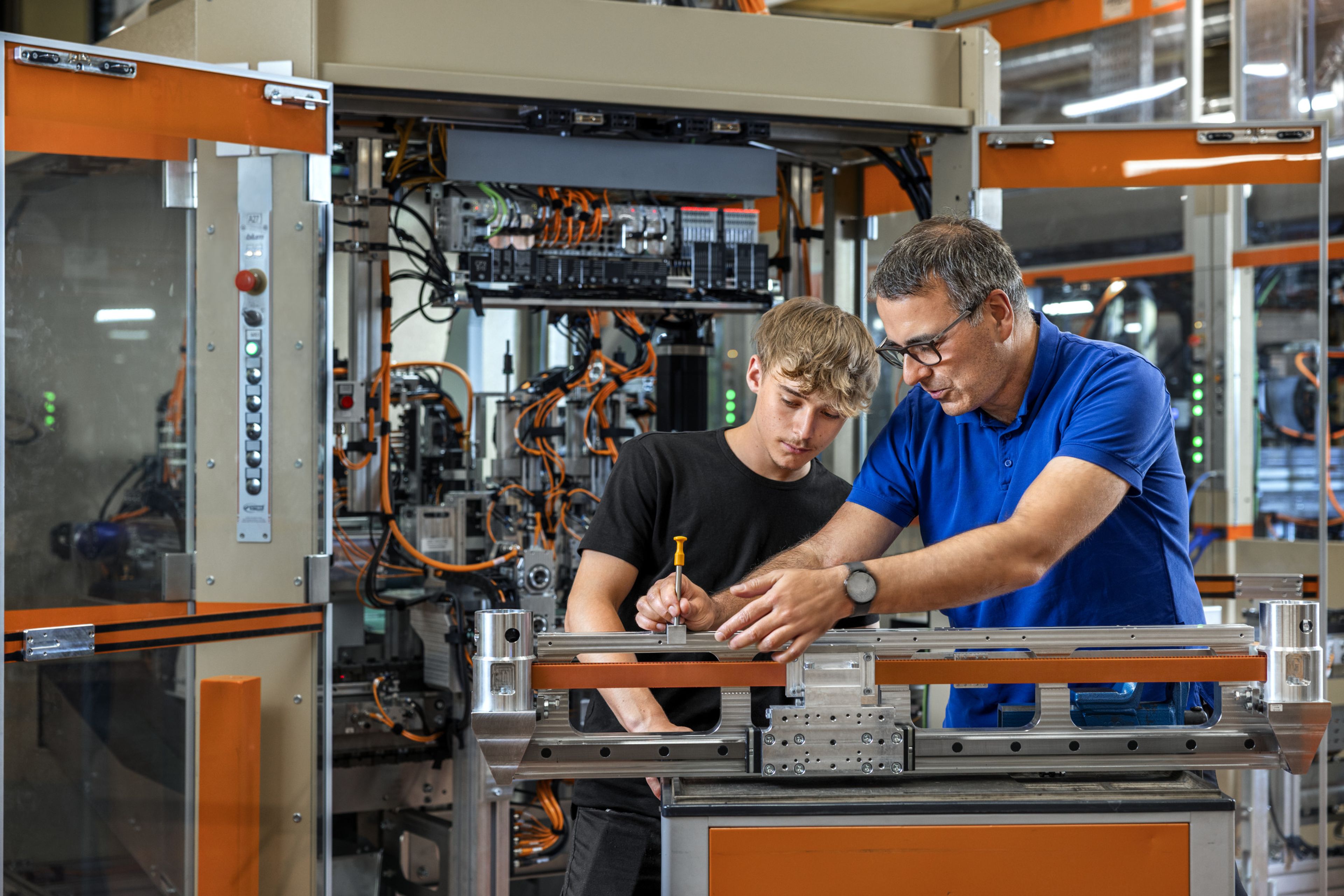 Das Bild zeigt einen Lehrling mit seinem Ausbilder die gerade die mechanischen Teile kontrollieren. 