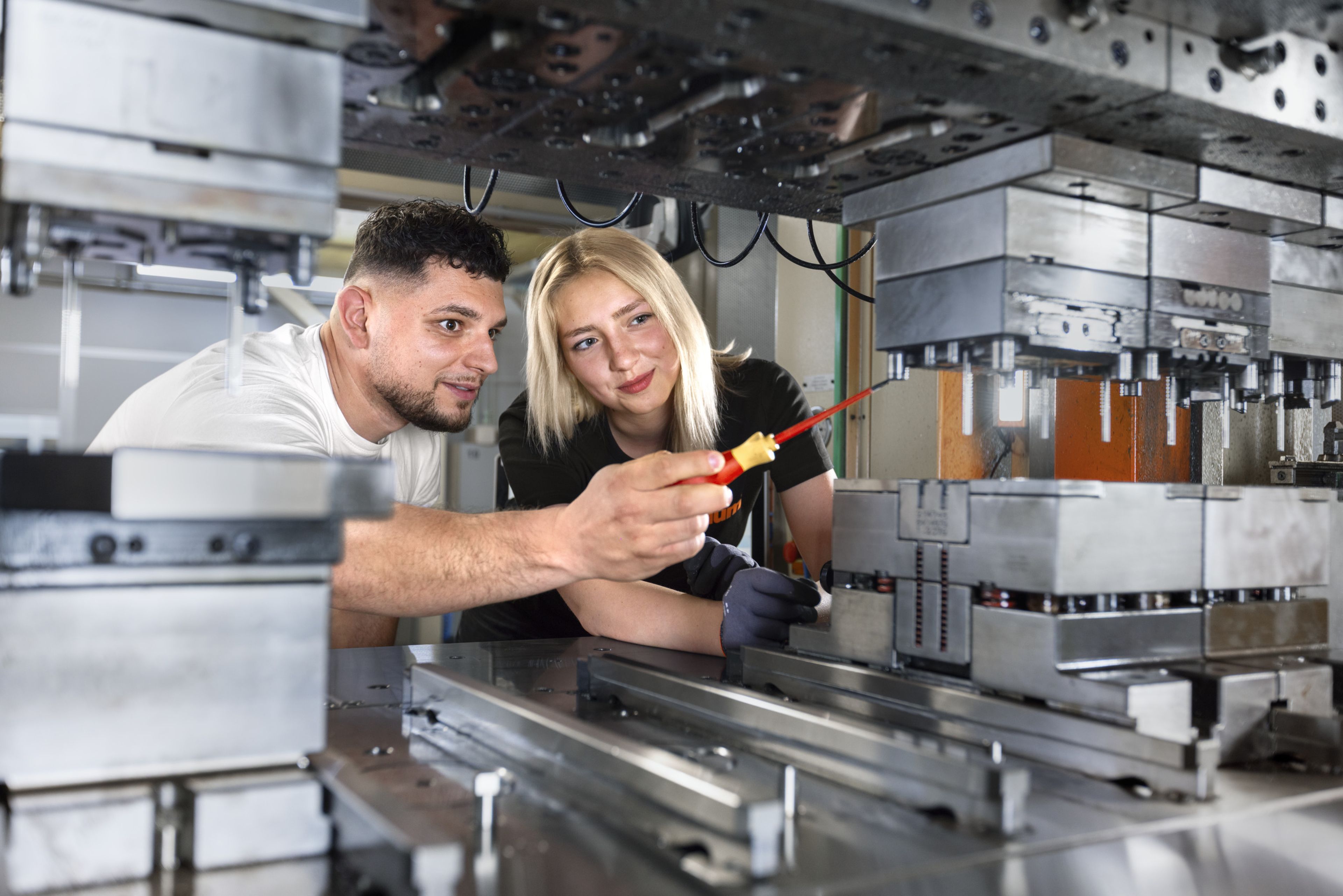 Das Bild zeigt einen Lehrling in der Prozesstechnik, wie sie gemeinam mit ihrem Ausbilder die Rüstung einer Stanze bespricht. 