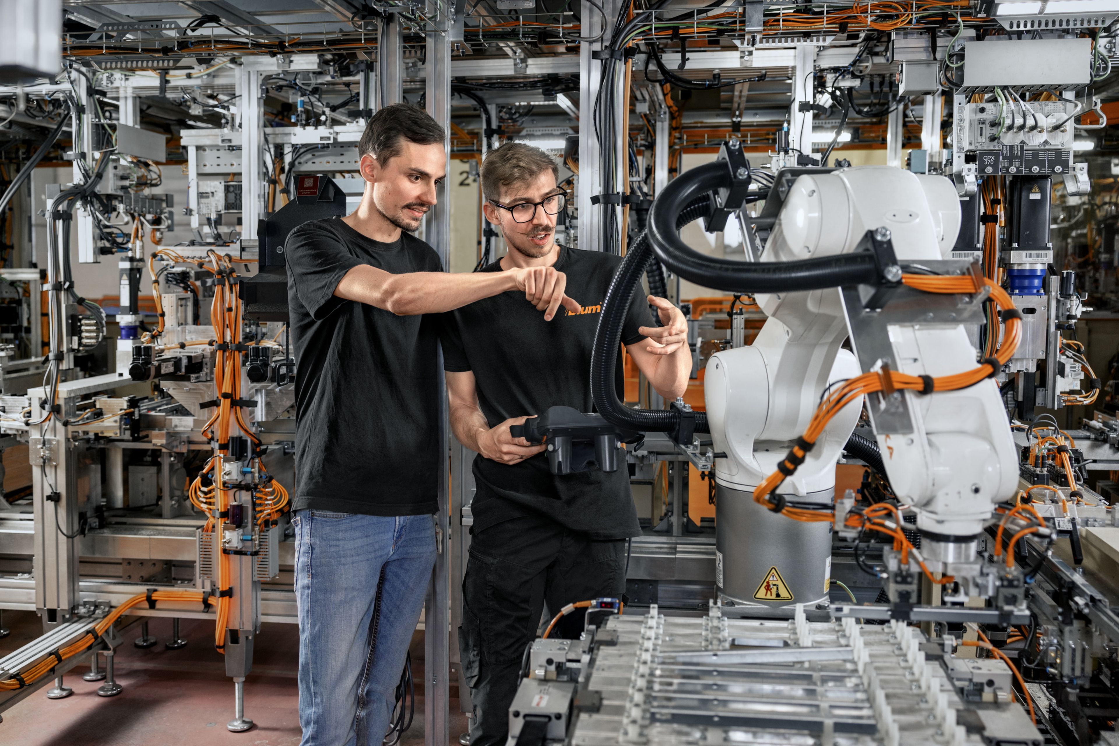 Das Bild zeigt einen Trainee mit seinem Ausbilder wie sie die funktionsweisen von einem Roboter in einer Anlage besprechen. 