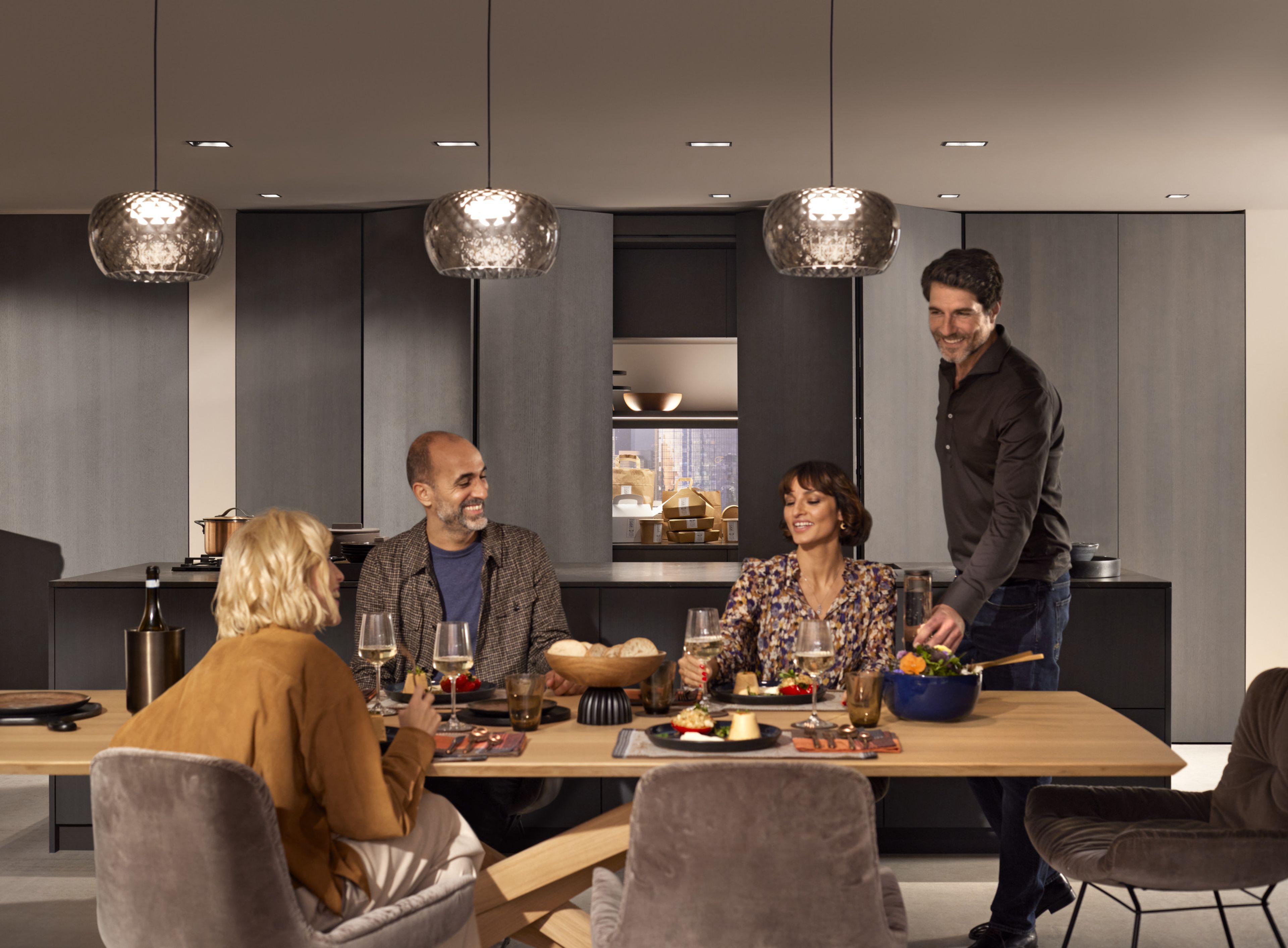 A group of people eats together at the table while takeaway containers on a kitchen run behind them are half-concealed by the REVEGO pocket system