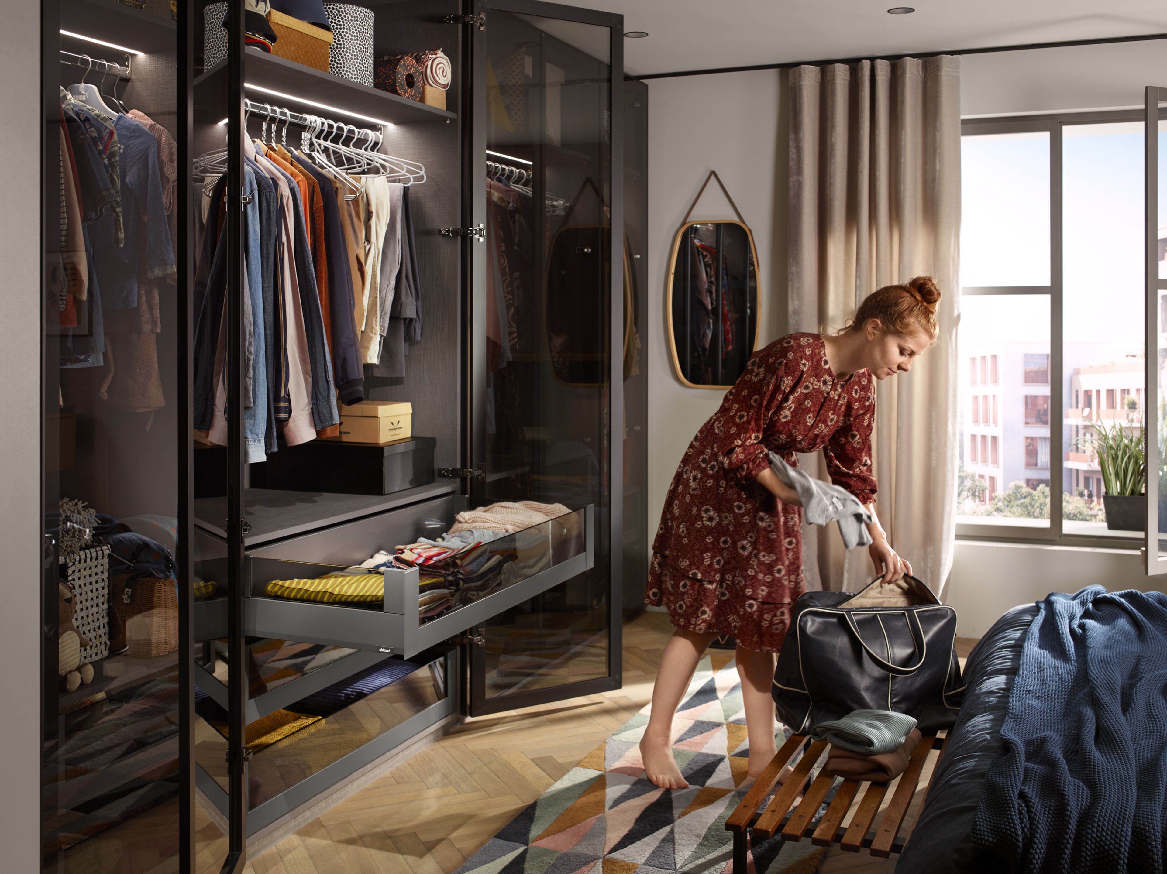 Eine Frau steht vor einem geöffneten Kleiderschrank mit MERIVOBOX-Schubladen und packt eine Tasche