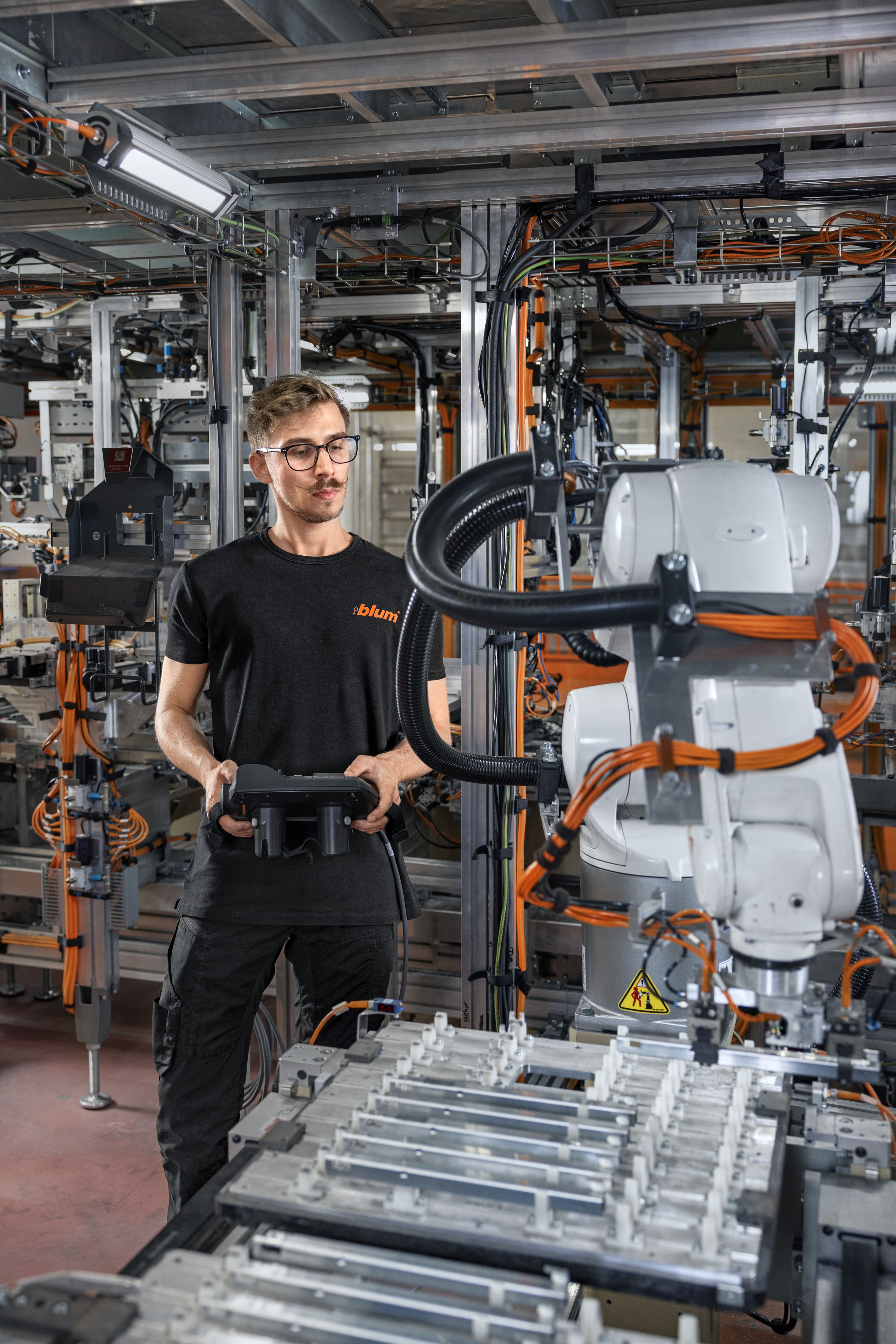 Auszubildender in der Dualen Akademie Mechatronik bedient einen Industrieroboter in einer automatisierten Fertigungsanlage mit Greifer und Werkstückträgern – Mensch-Roboter-Kollaboration in der industriellen Produktion.