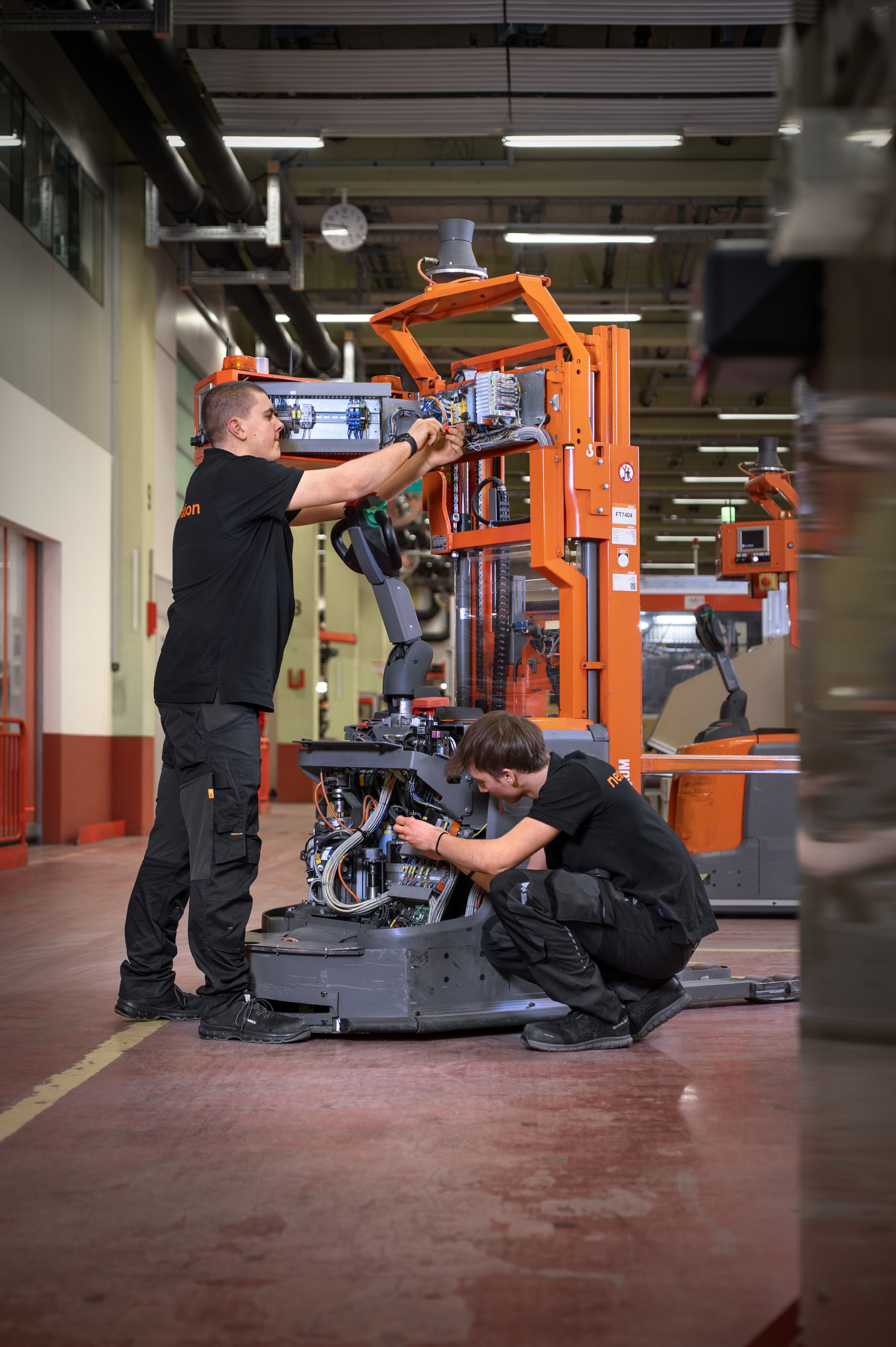 Auszubildende in der Mechatronik arbeiten an einer Anlage der Fördertechnik und montieren sowie verkabeln mechanische und elektrische Komponenten direkt im Produktionsumfeld.