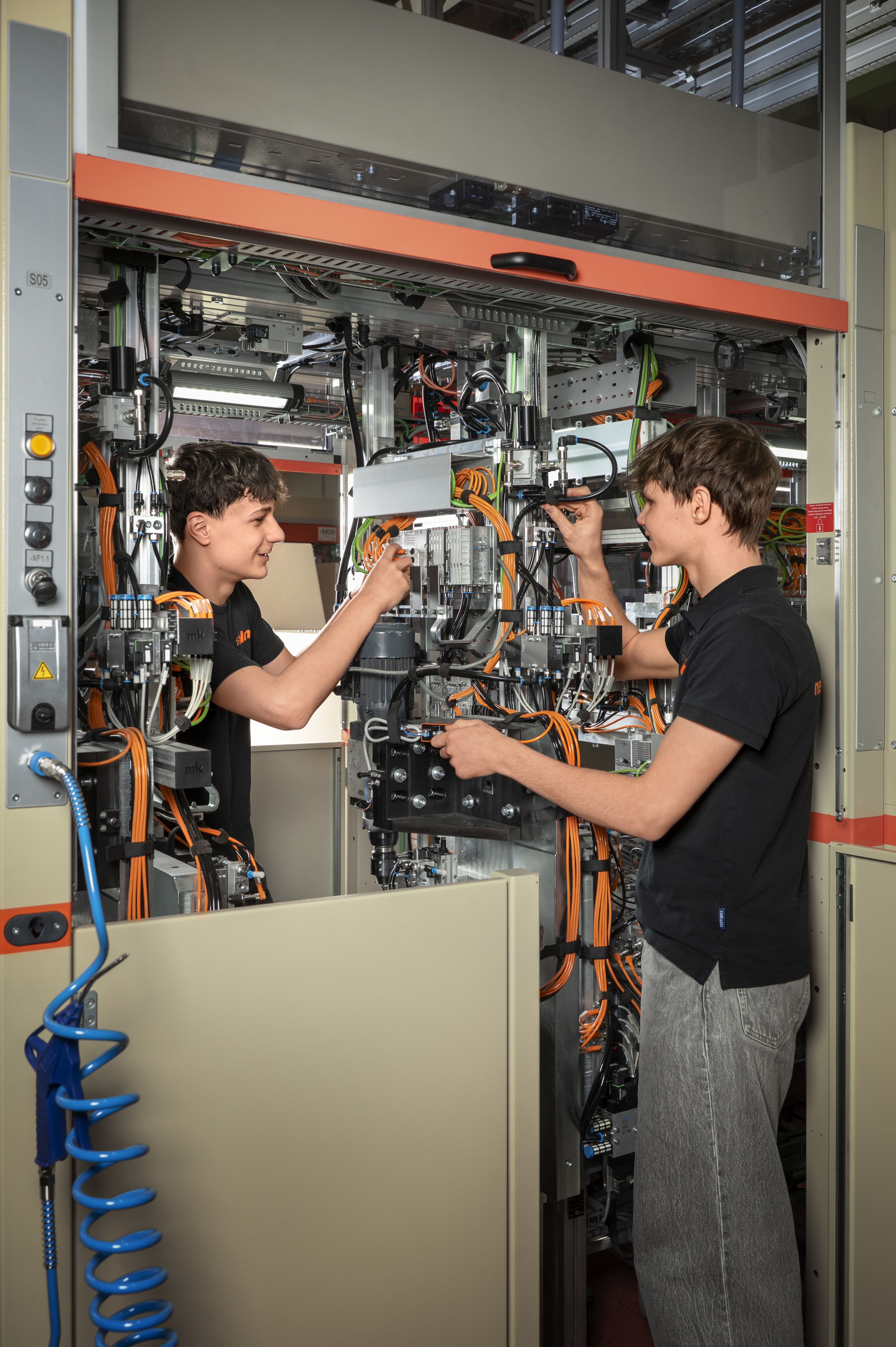 Zwei Lehrlinge in der Ausbildung Prozesstechnik bei Blum arbeiten an einer industriellen Produktionsanlage und montieren sowie prüfen elektrische und mechanische Komponenten.