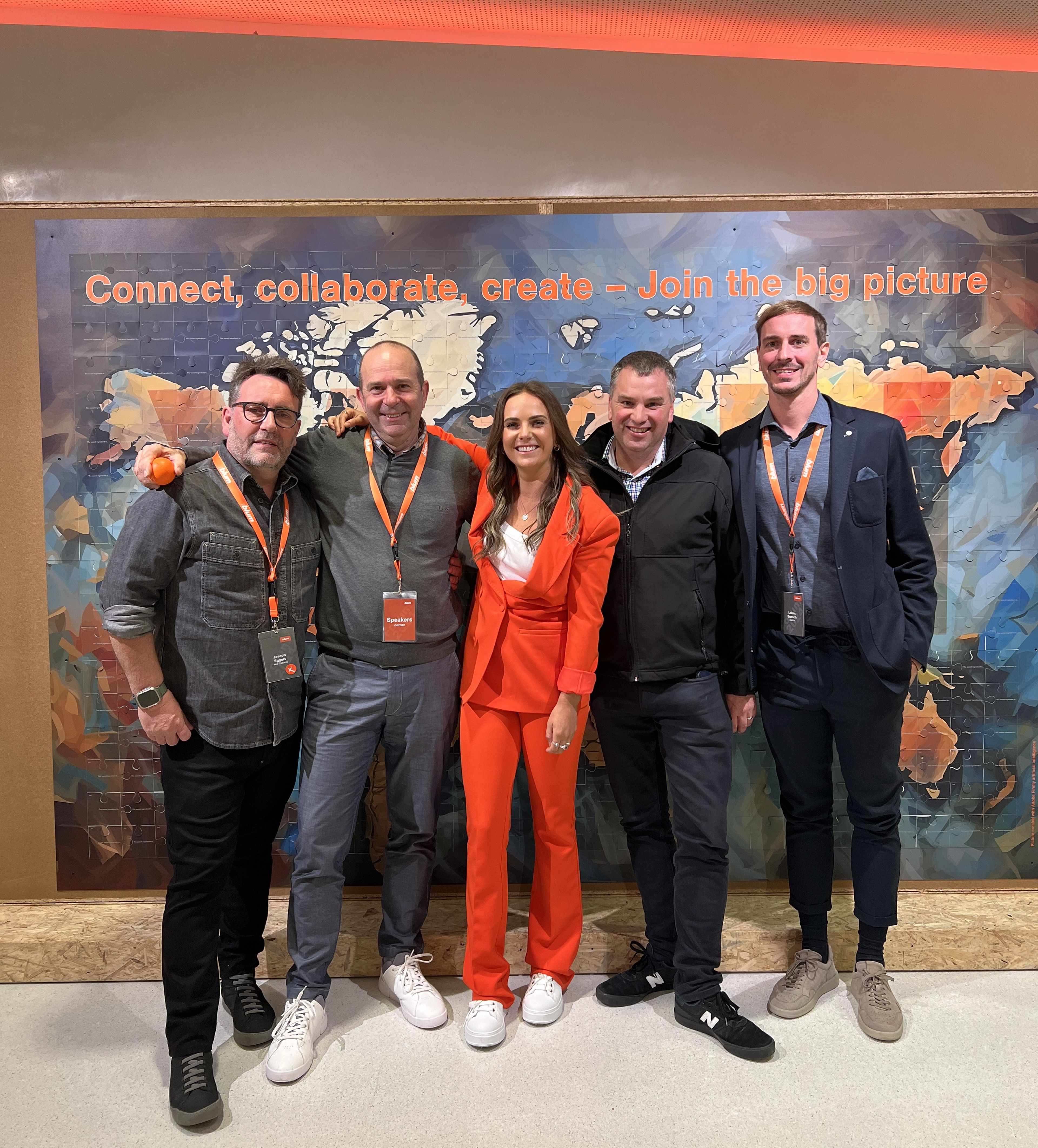 Five people smiling and standing in front of a colorful wall with a map and the slogan "Connect, collaborate, create – Join the big picture."