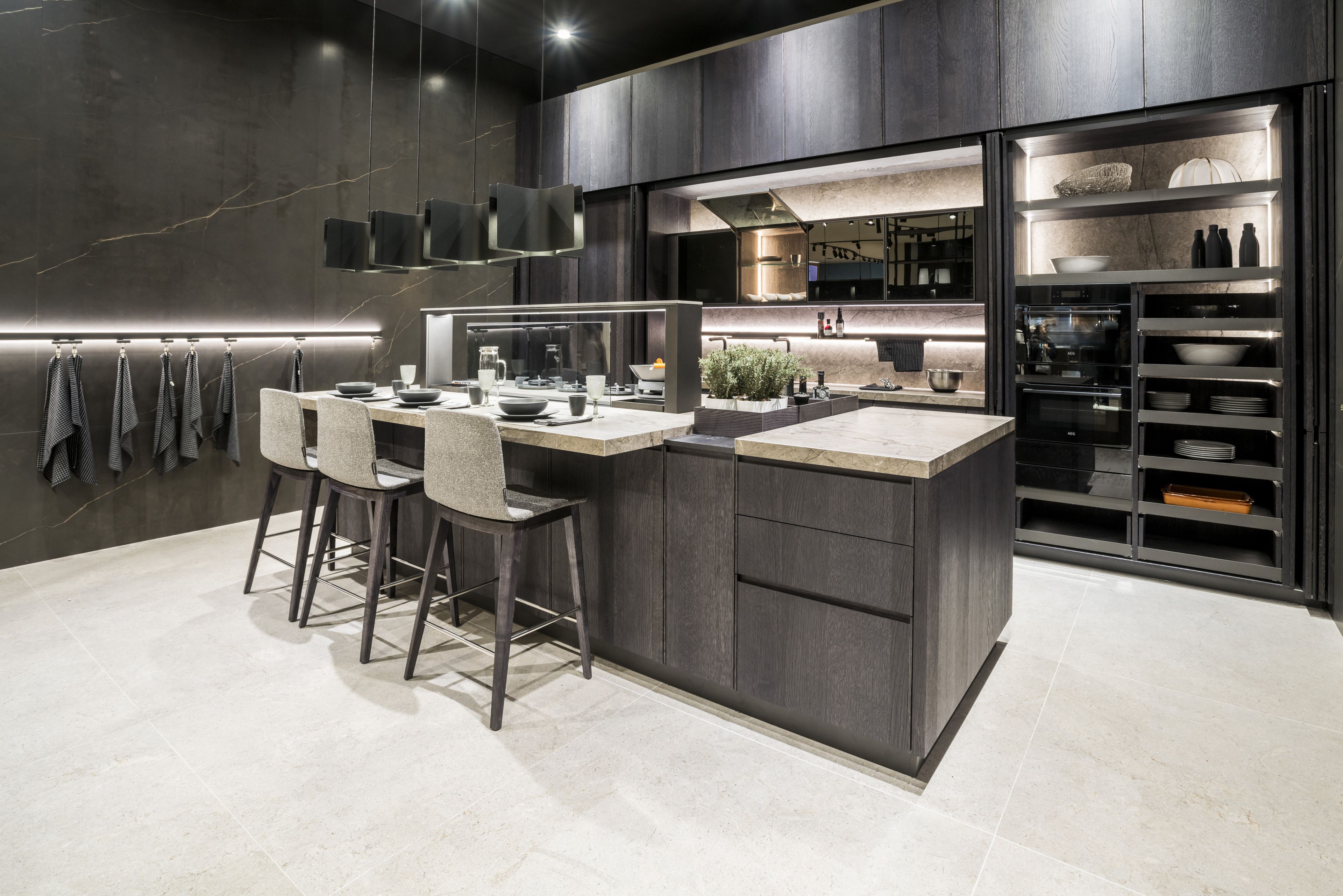 A dark-coloured island kitchen with a light work surface and glass elements