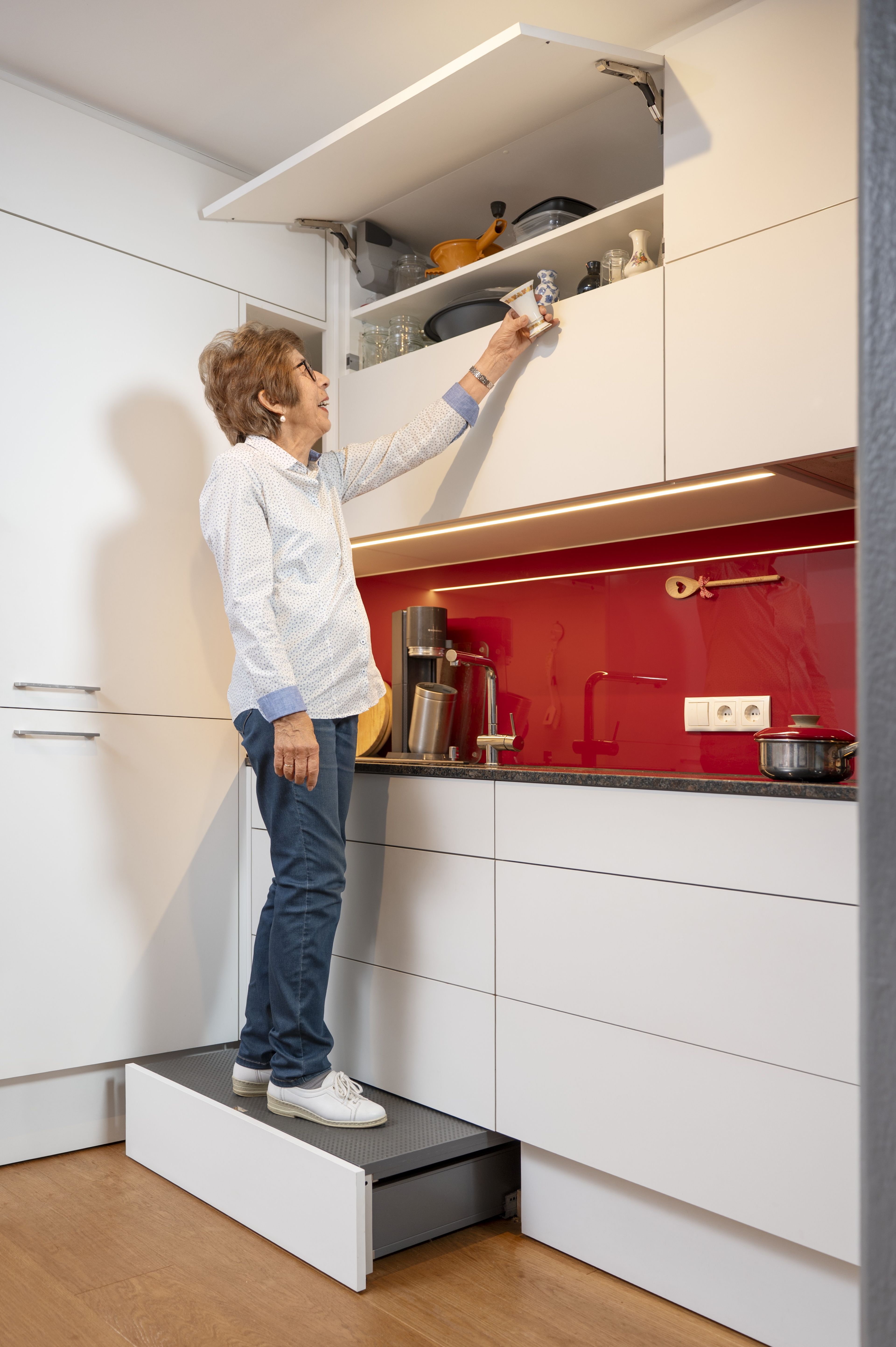 Eine Frau steht auf der Sockellösung SPACE STEP und entnimmt eine kleine Vase aus dem geöffnete Oberschrank