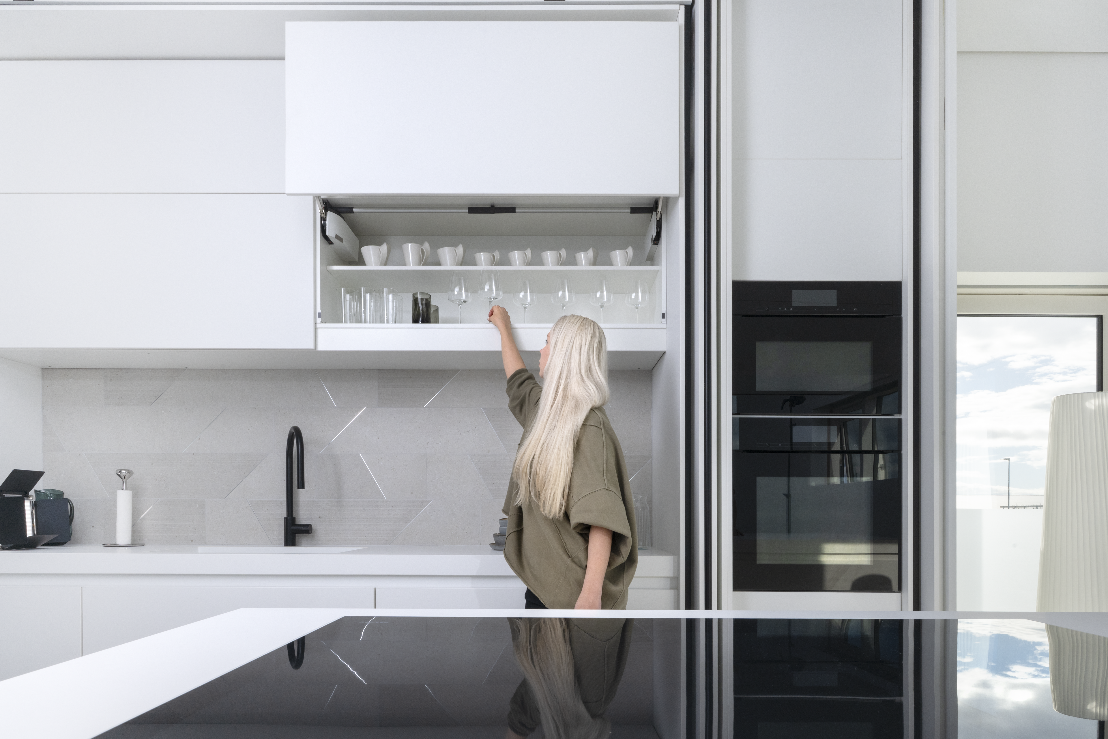 Eine Frau entnimmt ein Glas aus einem Oberschrank mit geöffnetem Klappensystem AVENTOS HL top