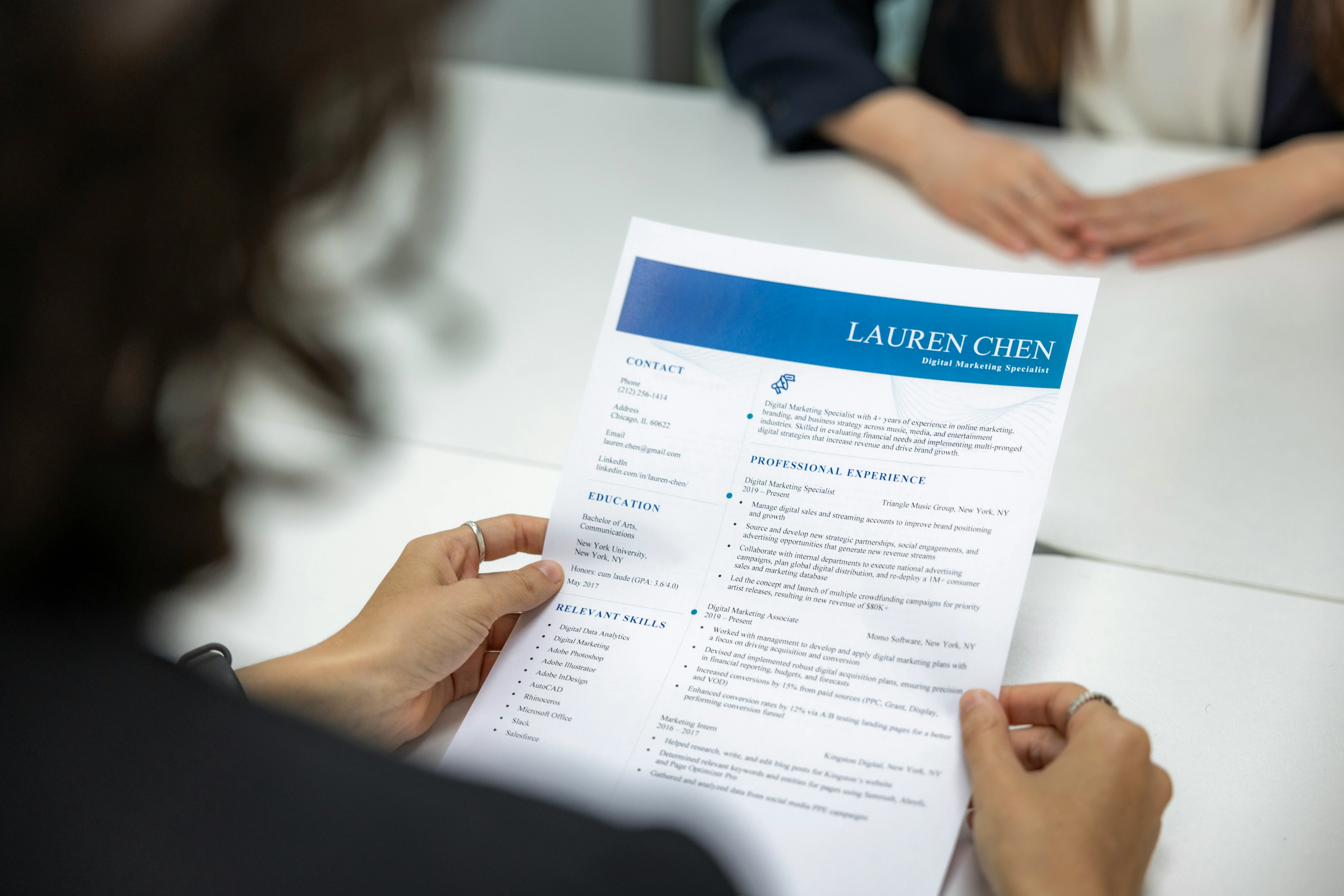 Person holding a resume during an interview, with focus on the document that includes sections on contact, education, and experience.