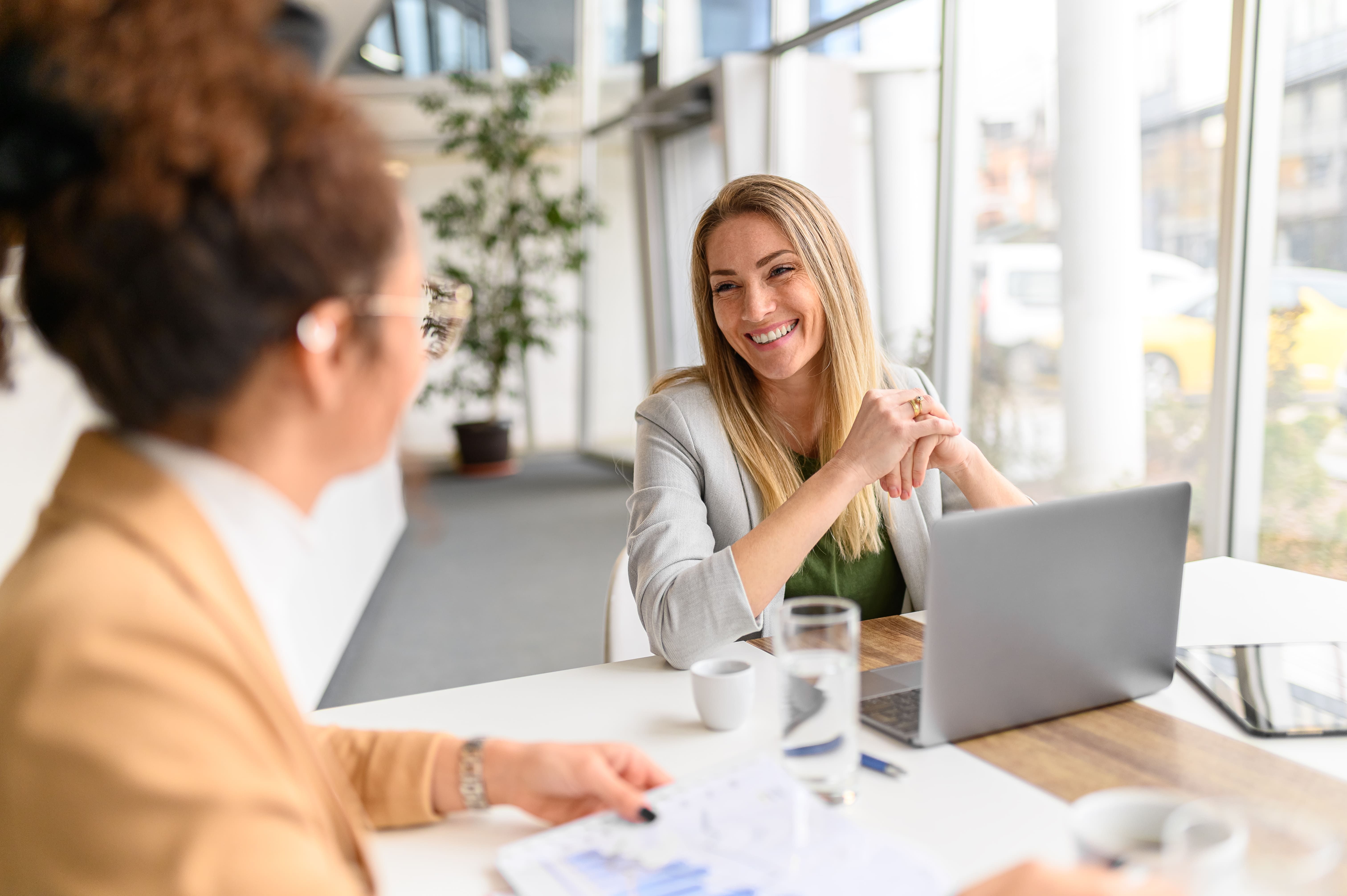 smiling businesswoman working laptop brainstorming business ideas with female coworker meeting