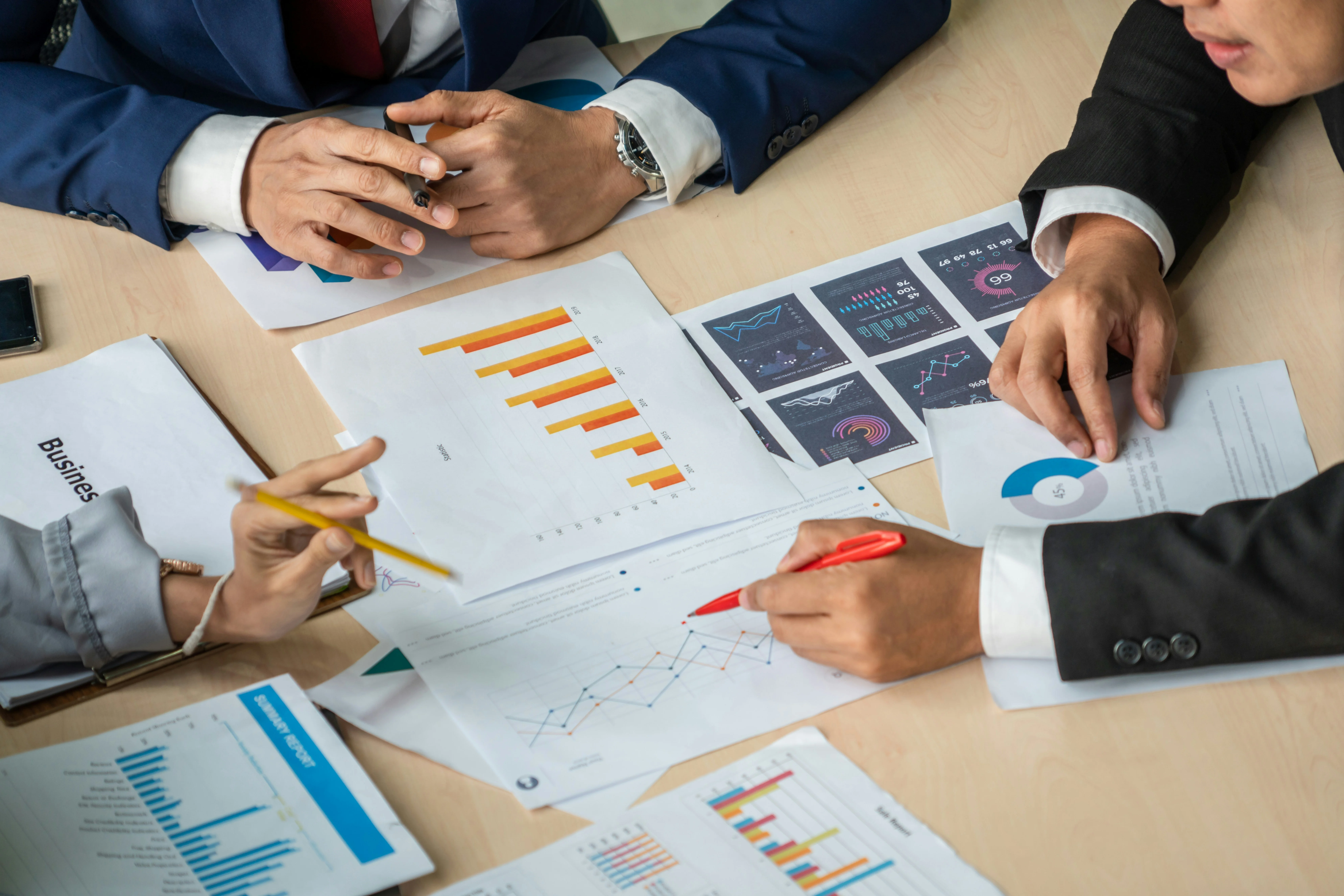 People discussing charts and graphs at a table, with documents showing bar and line graphs, and various data visualizations.