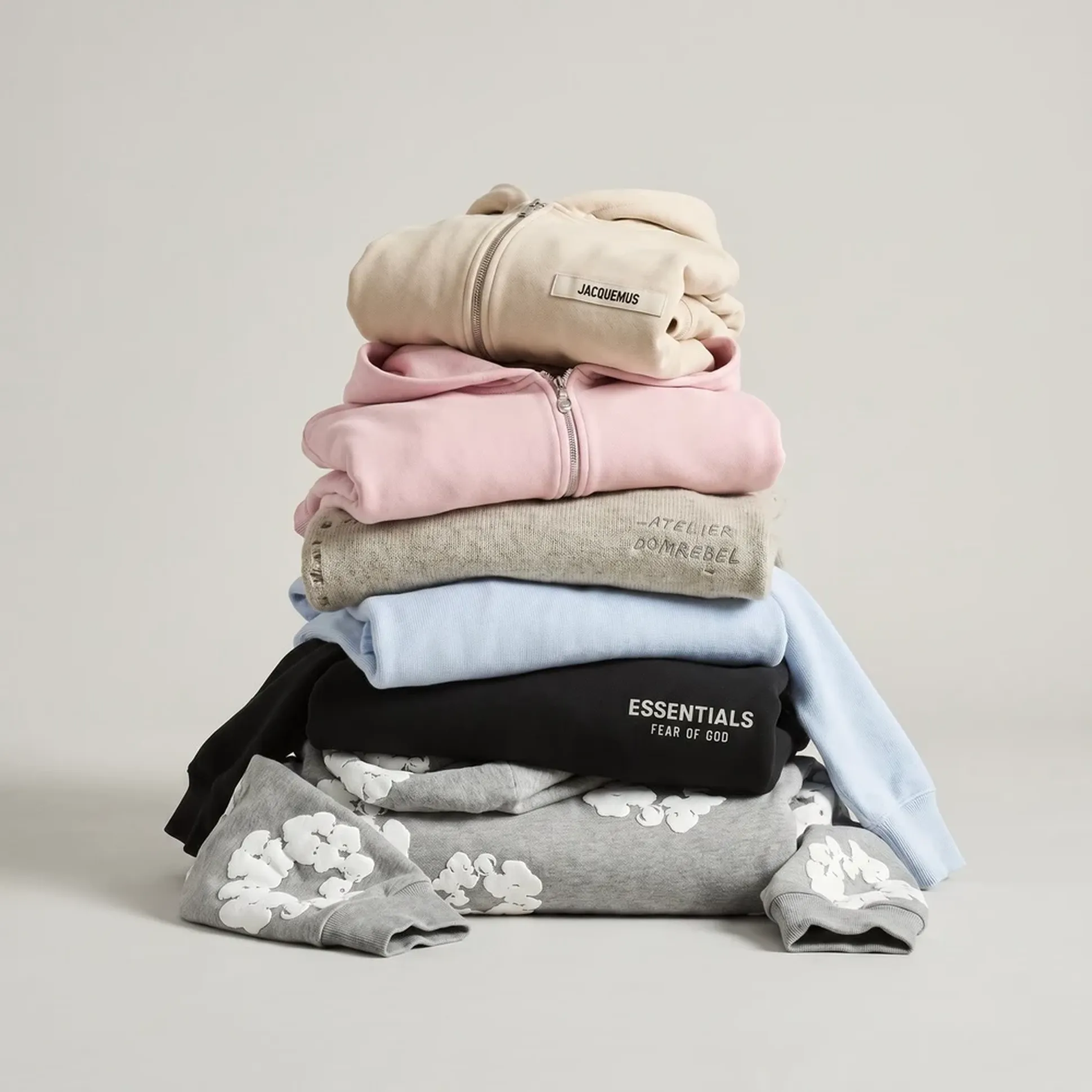 A stack of folded sweatshirts in various colors including beige, pink, grey, and blue, with visible brand labels and floral designs.
