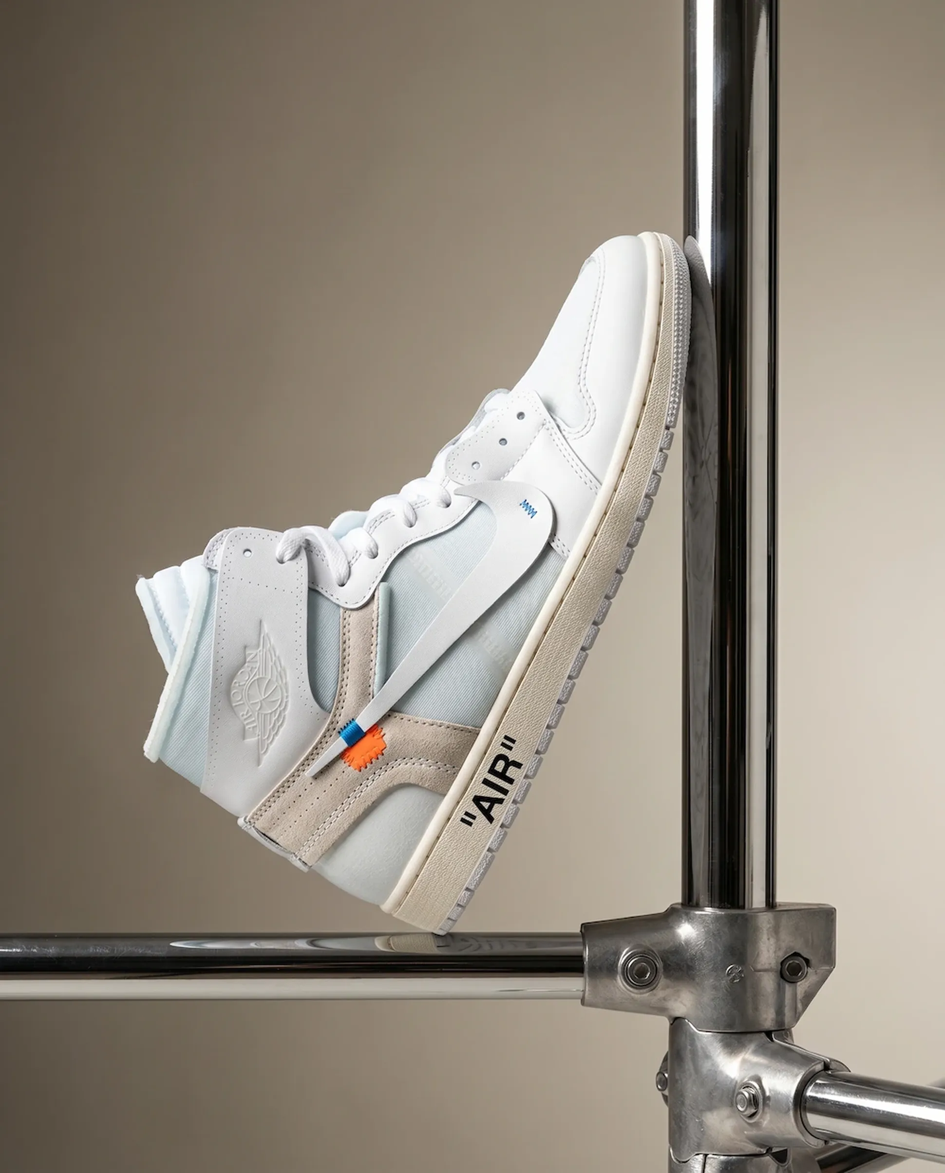 White and beige high-top sneaker with "AIR" text, positioned on a metal frame against a beige background.