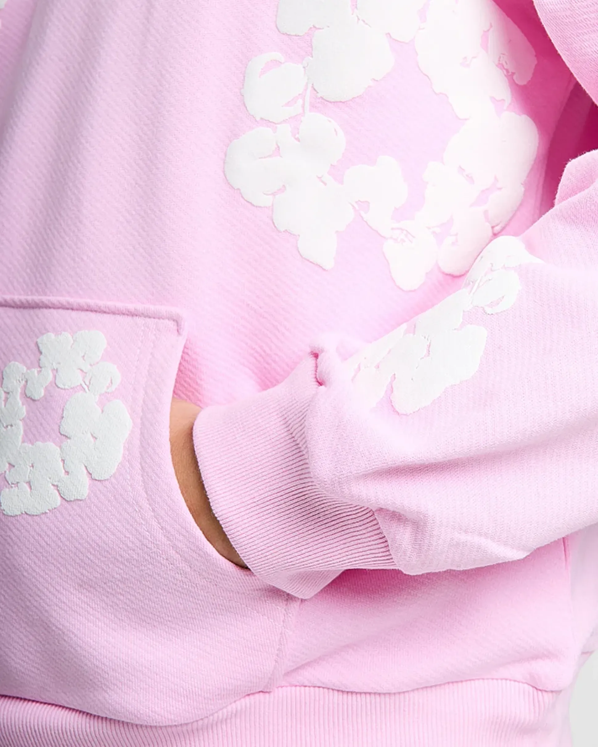 Close-up of a person wearing a light pink hoodie with white floral patterns. One hand is partially tucked into the front pocket.