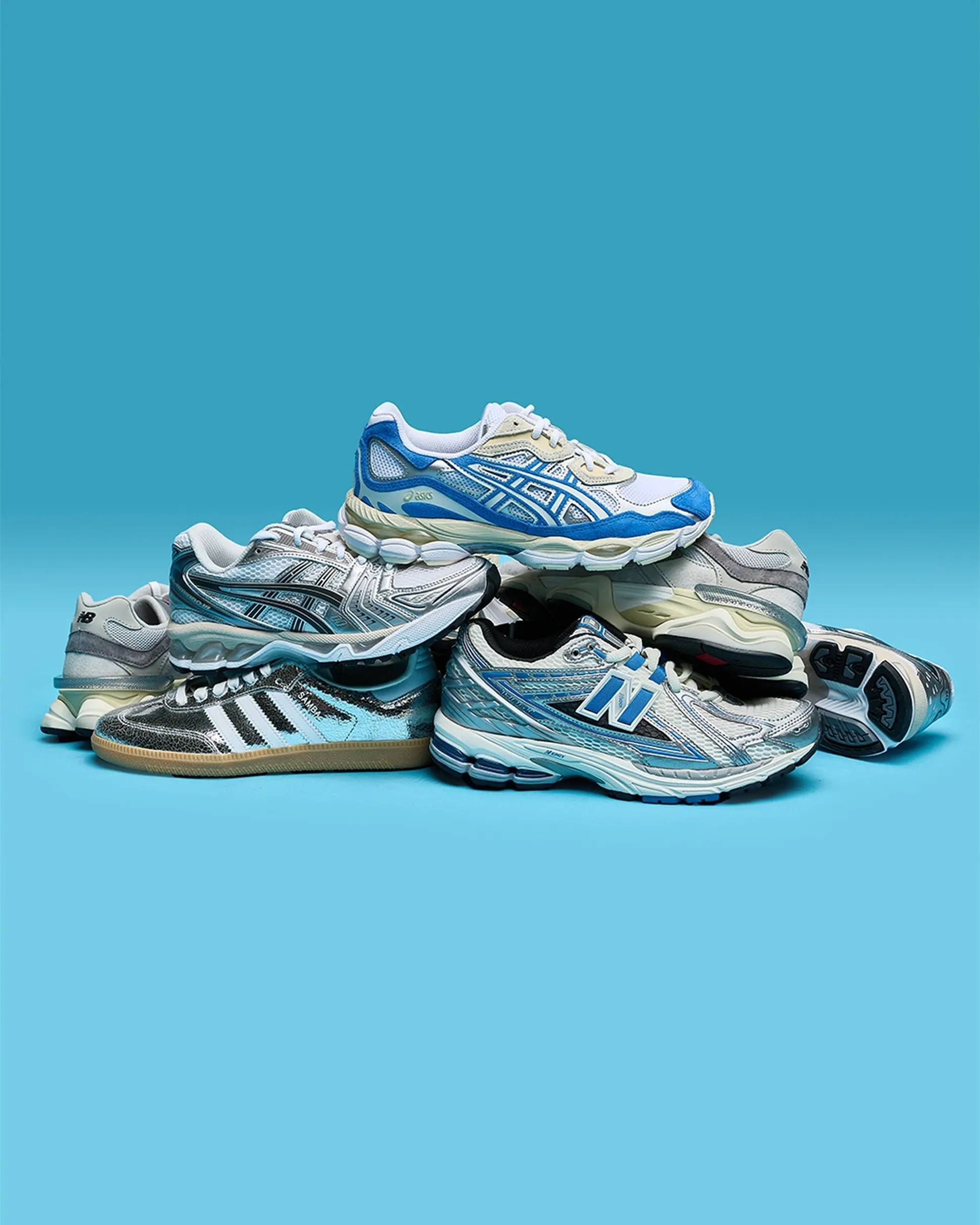 A pile of athletic sneakers in various styles and brands, featuring shades of blue, gray, and silver, against a blue background.