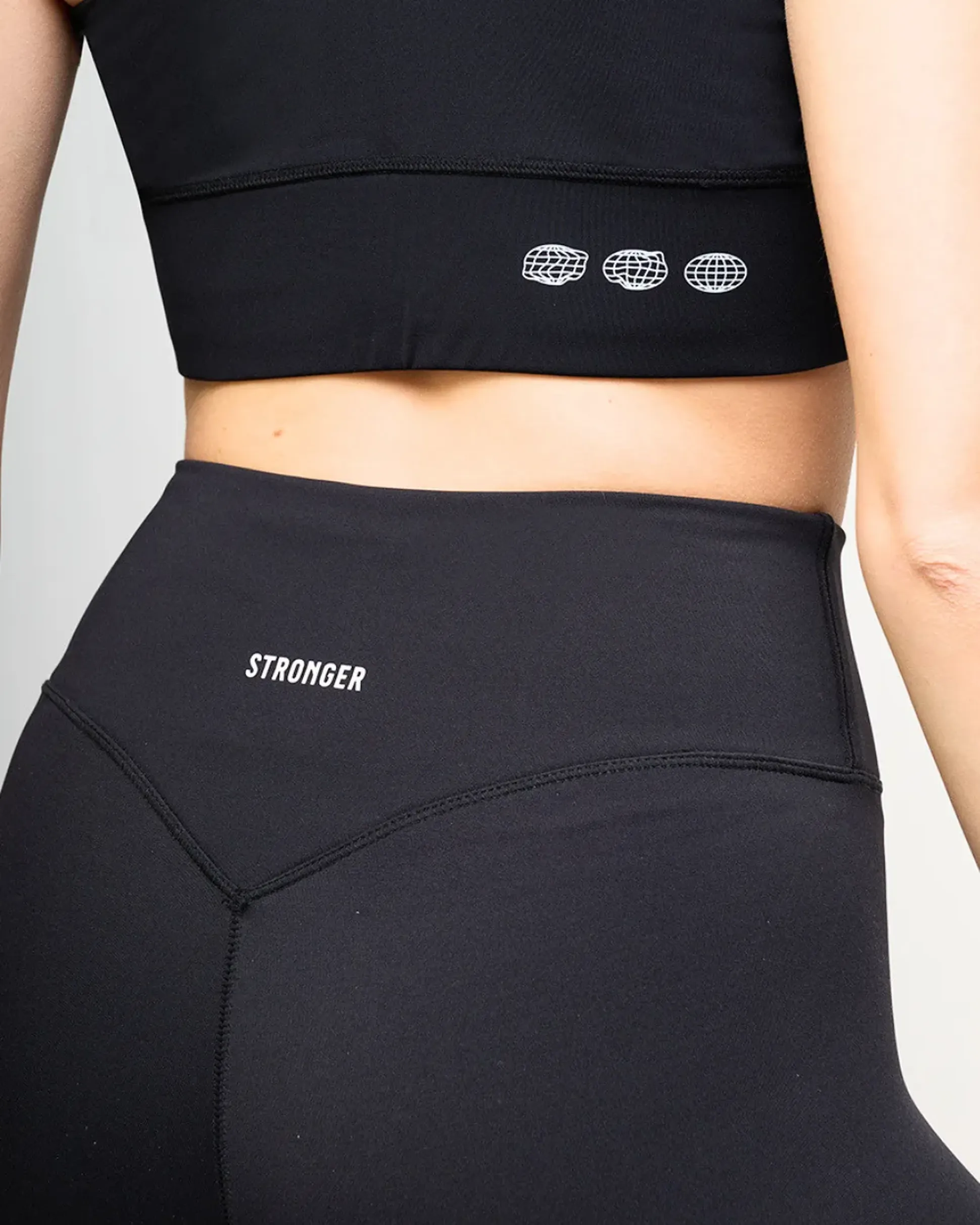 Person wearing black high-waisted leggings and a matching crop top with "STRONGER" printed on the leggings' waistband.