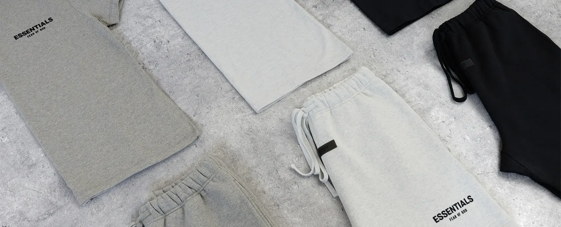 Flat lay of gray and black casual clothing, including T-shirts and joggers, on a textured gray surface.