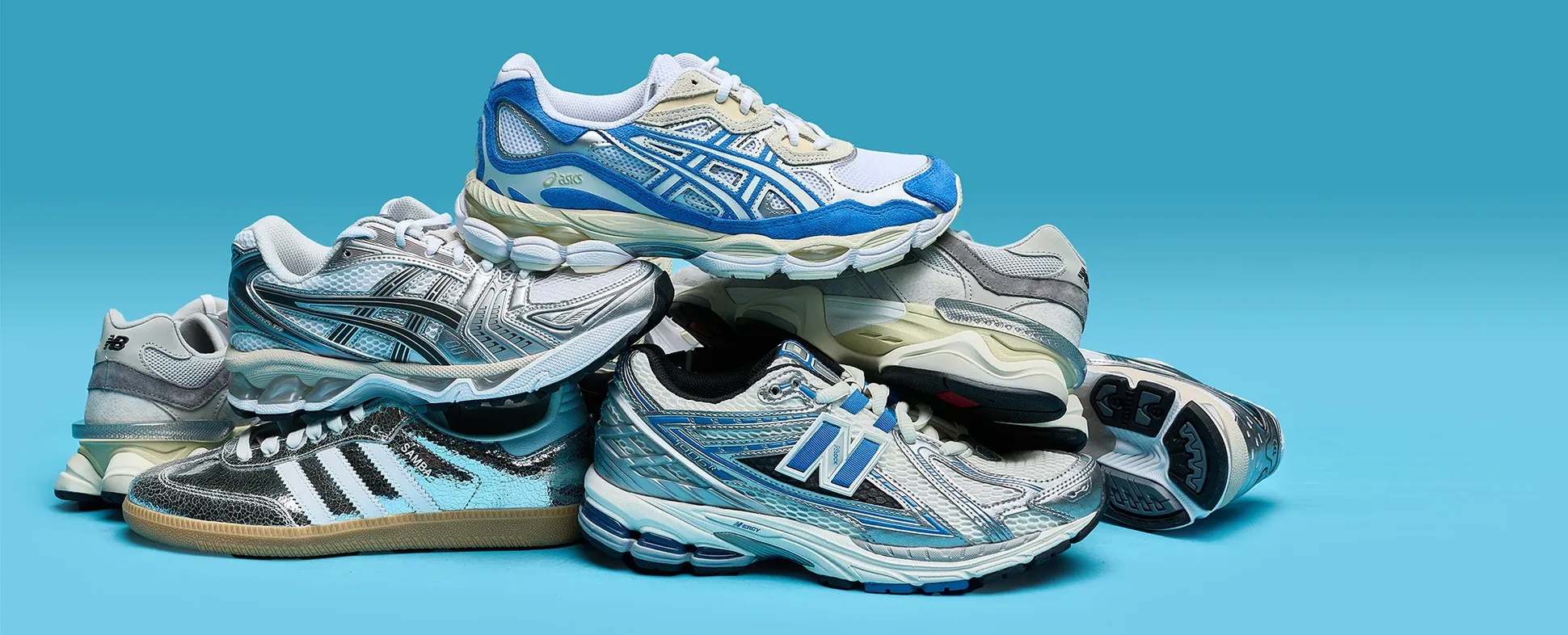 A pile of stylish athletic sneakers with various designs, including blue, silver, and white accents, against a solid turquoise background.