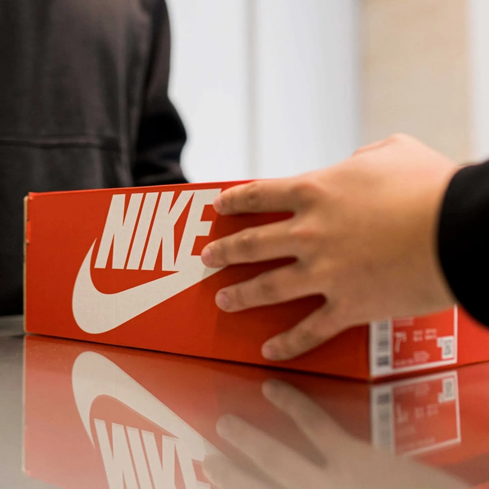 Person handing over an orange Nike shoe box across a reflective surface.