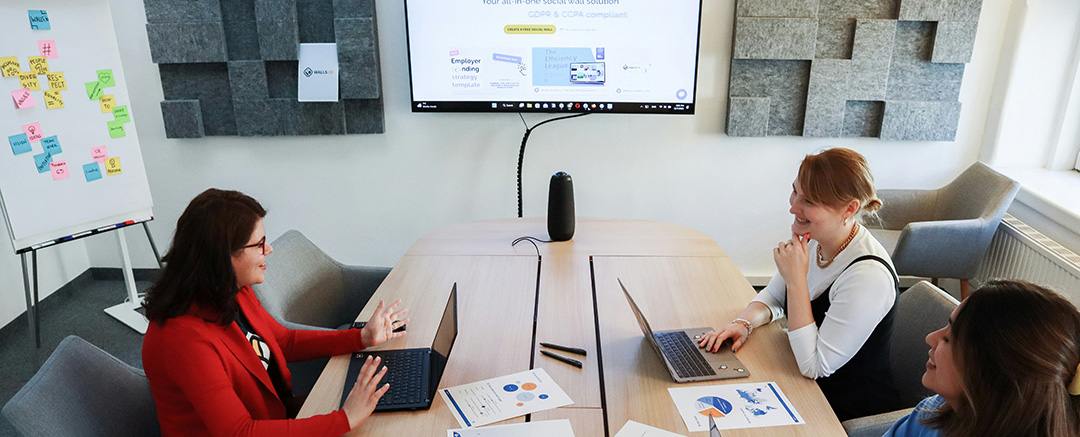 Team discussion in a modern meeting room with laptops and screen sharing, representing hybrid collaboration workflows and content sharing