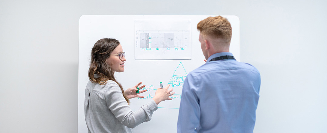 Two professionals discussing ideas on whiteboard illustrating physical collaboration surface with digital capture for hybrid meetings