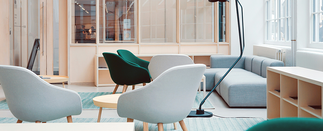 Modern lounge workspace A bright, modern workspace featuring soft-colored lounge chairs, a sofa, and wooden shelving, creating an open and inviting collaborative environment.