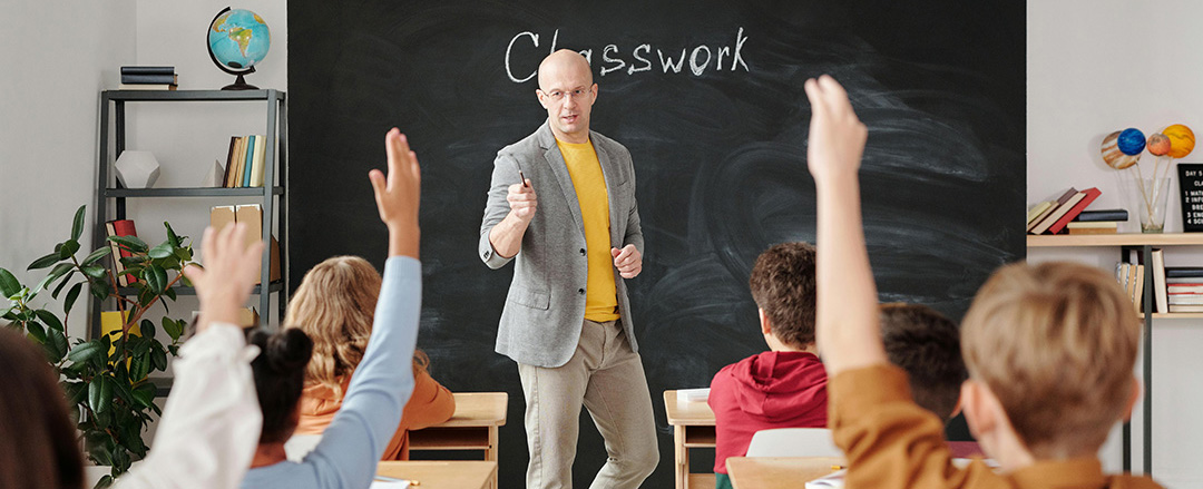 Teacher leading an active classroom lesson on a chalkboard with students raising hands, illustrating student engagement and traditional teaching methods in education