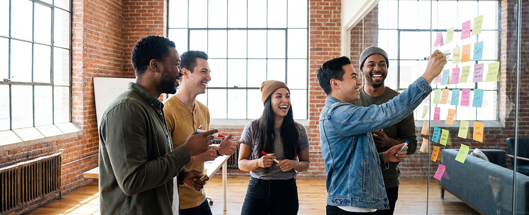 Diverse team brainstorming with sticky notes on a glass wall showing collaborative ideation and flexible workspace interaction
