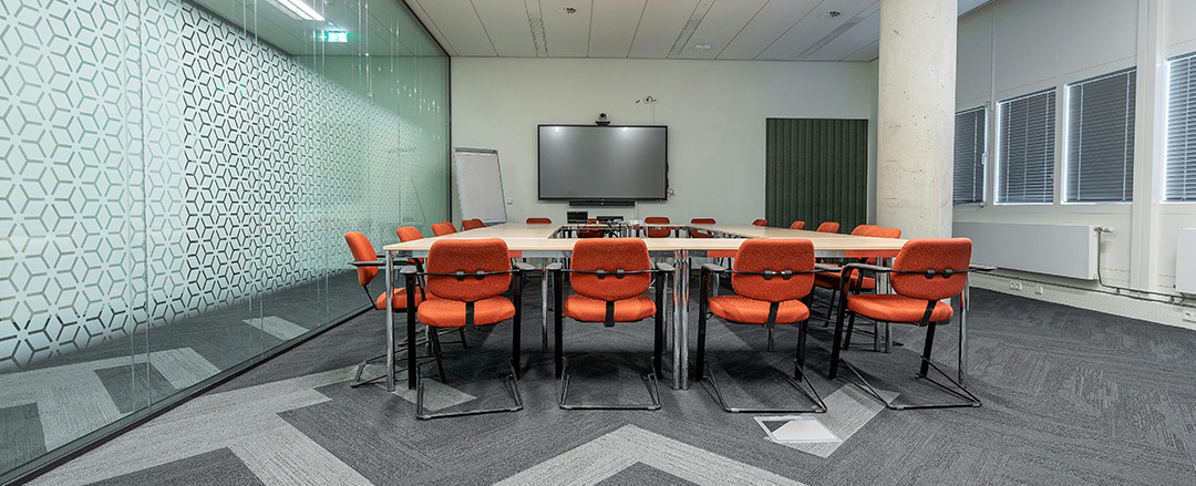 Team discussion in a modern meeting room with laptops and screen sharing, representing hybrid collaboration workflows and content sharing