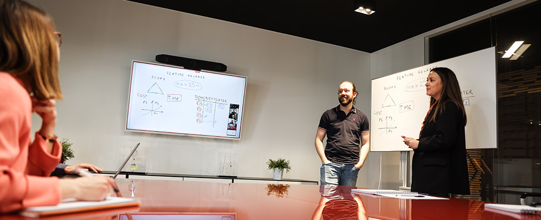 Team in a hybrid meeting using a digital whiteboard and physical whiteboard illustrating scalable collaboration and real-time idea sharing across in-room and remote participants