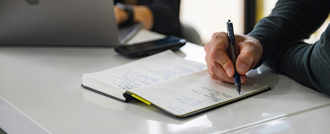 Close-up of a person writing in a notebook representing analog-to-digital collaboration and personal ideation phase