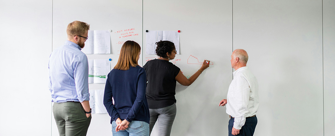 Team collaborating on whiteboard surface in modern meeting room representing collaborative workflows and hybrid-ready interaction