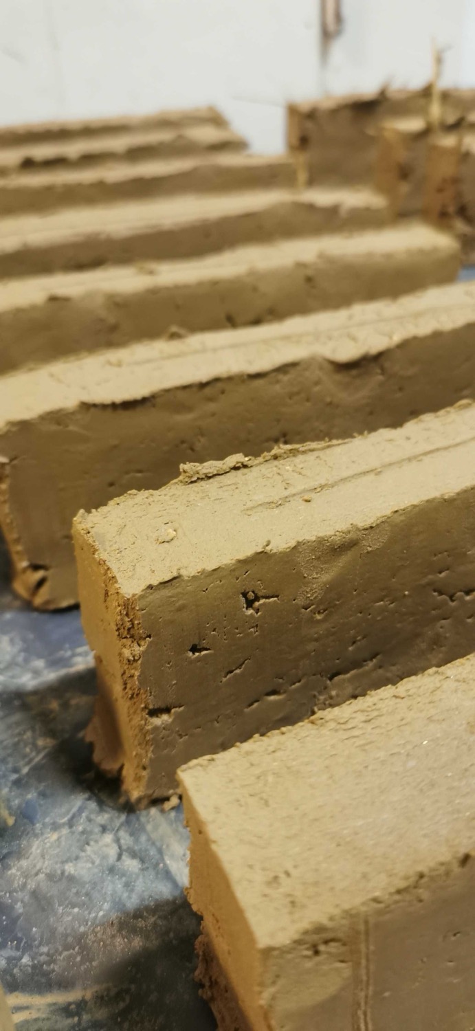 Close-up of several rectangular adobe bricks drying on a plastic surface, showing rough textures and earthy brown color.