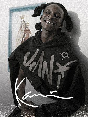 Smiling person with braided hair, wearing a black hoodie with graffiti-style text, stands in front of a framed religious painting, signature below.