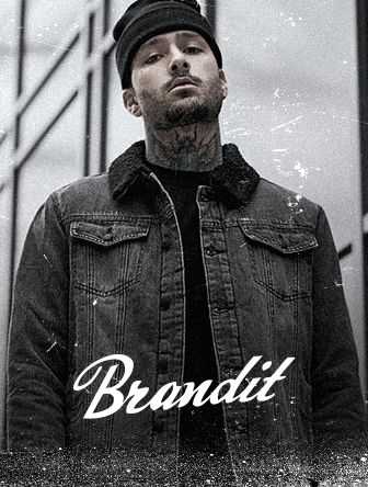 Man in a denim jacket and beanie, with tattoos, stands in front of a building with "Brandit" text overlay.