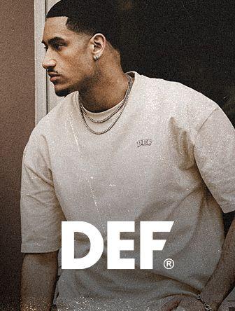 Man wearing a beige DEF t-shirt, looking to the side, with short hair and a chain necklace. DEF logo is prominently displayed at the bottom.