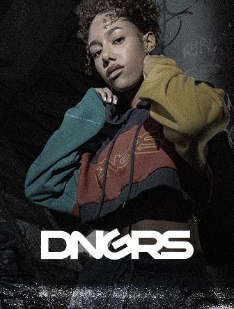 Person in a stylish, multi-colored hoodie poses confidently, with the text "DNGRS" below. Graffiti-covered wall in the background.