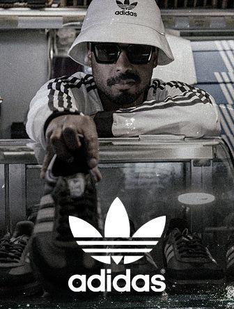 A person wearing a white Adidas hat and sunglasses leans over a glass case filled with Adidas shoes, with the Adidas logo prominently displayed.