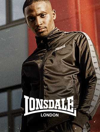A person wearing a black Lonsdale tracksuit poses confidently outdoors with a building in the background.