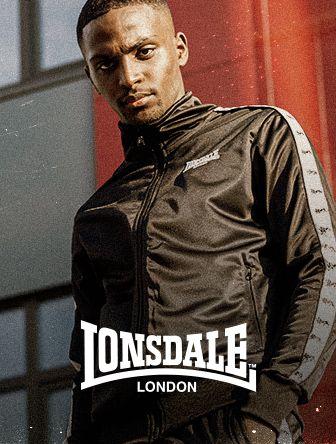 A person wearing a black Lonsdale tracksuit poses confidently outdoors with a building in the background.
