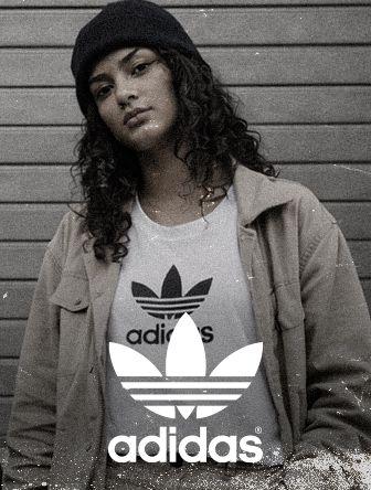 Person in a beanie and jacket over an Adidas t-shirt stands against a striped background, with a vintage photo effect.