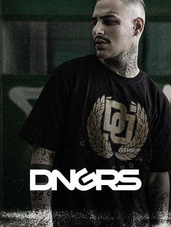 Man with tattoos wearing a black DNGRS shirt and looking sideways, standing against a green background.