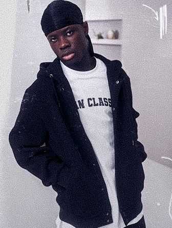 Young man wearing a black hoodie, white T-shirt, and black durag, stands in a minimalistic room with a calm expression.