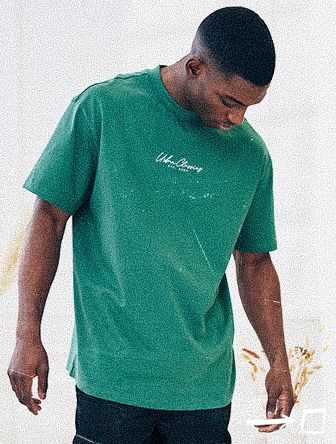 Man wearing a green T-shirt with white text, looking down, standing against a light background.
