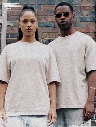 Two people in matching beige outfits stand side by side against a brick wall. One wears sunglasses, and both have a serious expression.