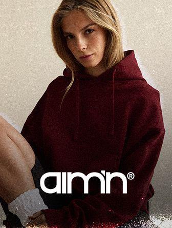 Person sitting with legs crossed, wearing a maroon hoodie and white socks. The word "aim'n" is visible at the bottom.