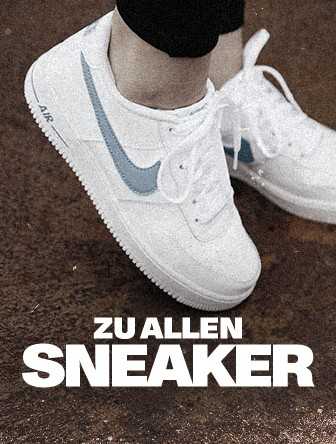 White sneakers with blue swoosh and "AIR" on the sole worn by a person, standing on a textured brown surface. Text reads "ZU ALLEN SNEAKER."