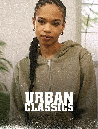 Person in a gray hoodie with braided hair stands indoors. Text reads "Urban Classics."